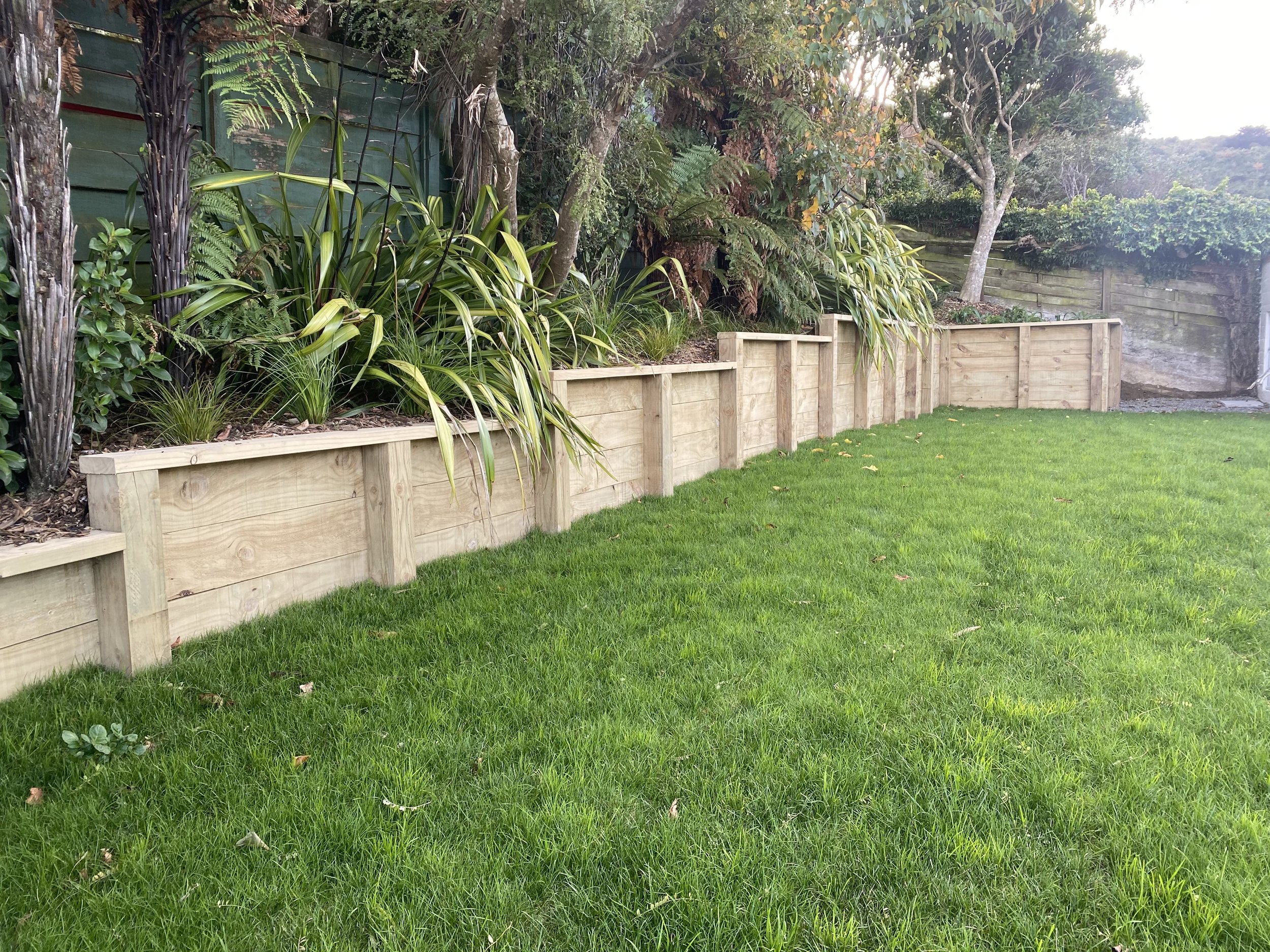 A well-designed tiered timber retaining wall in a lush Wellington garden setting.